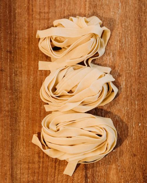 Three nests of uncooked fettuccine pasta arranged on a wooden surface.