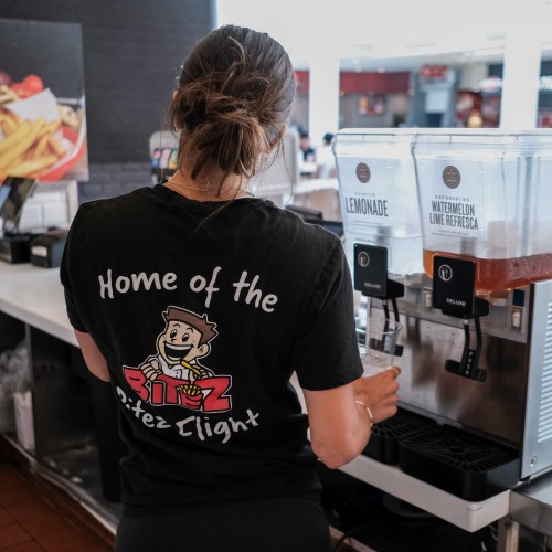 A person in a black t-shirt stands at a drink station, preparing a beverage at a fast-food restaurant.