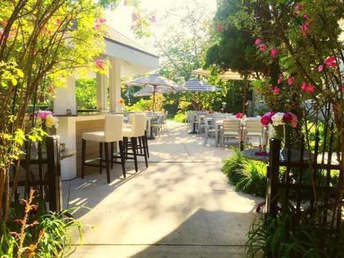 A sunny outdoor dining area with tables, chairs, and vibrant flowers lining the pathway.