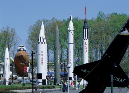 A display of various rockets and missiles, including a Saturn V, set in a park with trees in the background.