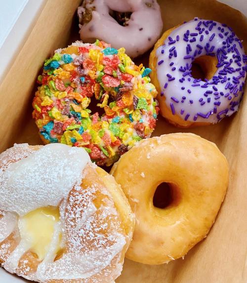 A box of assorted donuts: one with colorful cereal, one with purple sprinkles, a glazed donut, and two filled donuts.