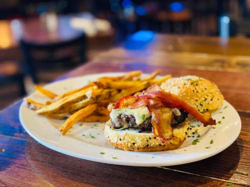 A juicy burger topped with bacon and cheese, served with a side of crispy fries on a white plate.