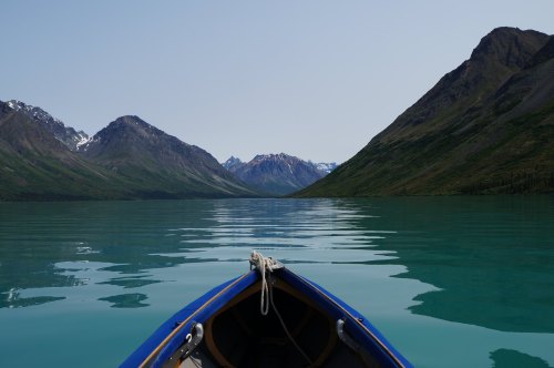 A view from a boat on calm turquoise water, surrounded by mountains under a clear sky.