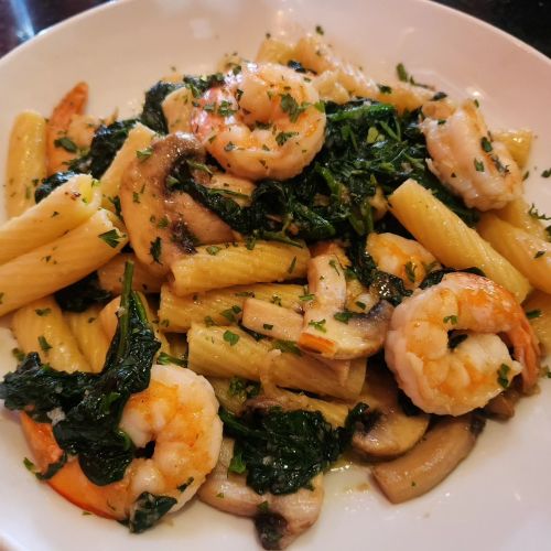 A plate of pasta with shrimp, spinach, and mushrooms, garnished with herbs.