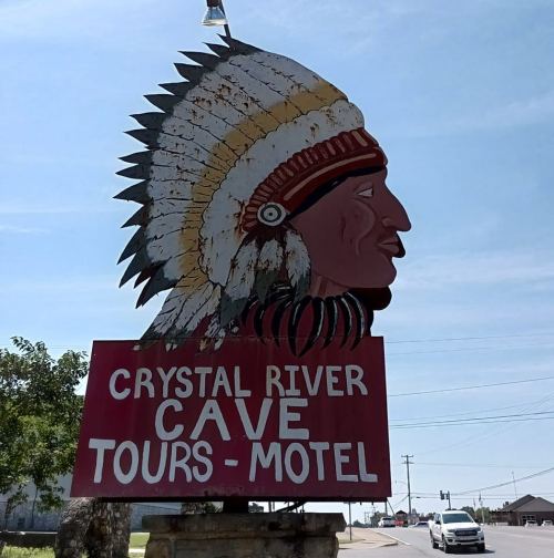 Sign featuring a Native American chief's head with text: "Crystal River Cave Tours - Motel." Roadside setting.