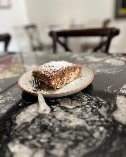 A slice of dessert dusted with powdered sugar on a plate, resting on a marble table.