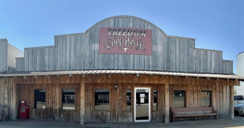 A rustic wooden building with a sign reading "Freedom Chop House" and a covered porch. Clear blue sky above.