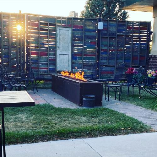 A cozy outdoor seating area with a fire pit, surrounded by wooden fencing and greenery, illuminated by sunset.