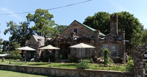 A unique stone house with a green roof, surrounded by trees and gardens, featuring outdoor umbrellas for seating.