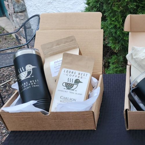 Two gift boxes containing coffee mugs and bags of coffee, labeled "Loons Nest Coffee" and "Carlson."