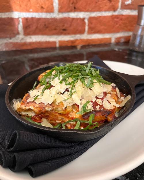A serving of lasagna topped with fresh basil and grated cheese, presented on a black plate with a napkin.