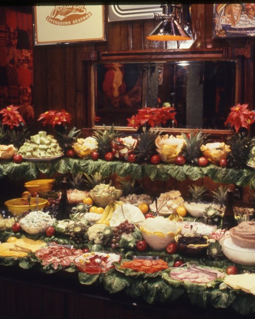 A vibrant buffet display featuring an array of fruits, salads, and seafood, decorated with festive greenery and flowers.