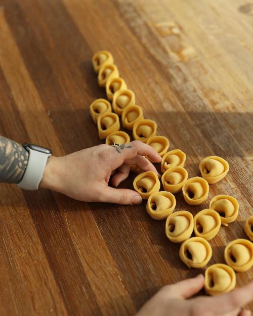 A hand arranging neatly shaped pasta on a wooden surface, showcasing a row of filled pasta pieces.