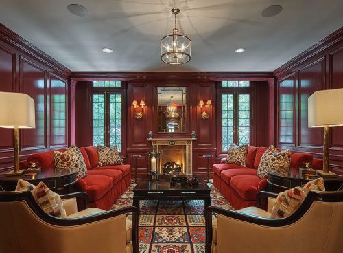 Cozy living room with red walls, plush sofas, decorative pillows, a fireplace, and elegant lighting.
