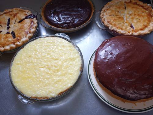 A variety of baked pies and a chocolate cake on a countertop, showcasing different flavors and textures.
