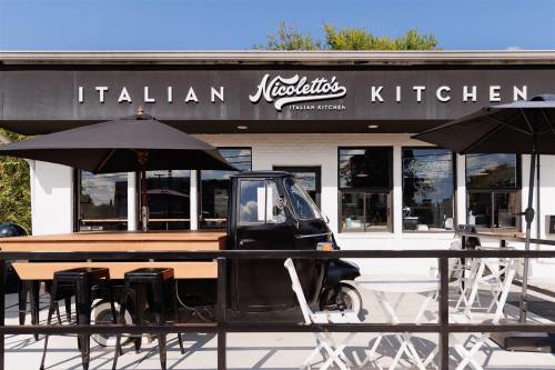 Exterior of Nicoletto's Italian Kitchen featuring a food truck, outdoor seating, and a clear blue sky.
