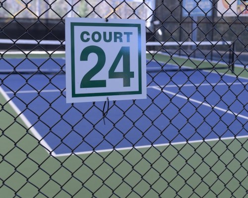Sign reading "Court 24" on a fence in front of a blue tennis court.