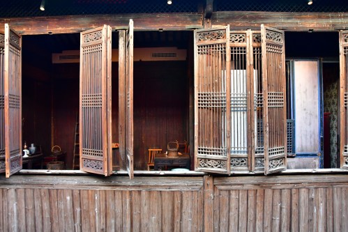 Wooden windows open to reveal a rustic interior with traditional furniture and decor.