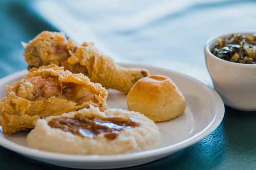 A plate of fried chicken, a biscuit, creamy grits with gravy, and a side of greens in a small bowl.