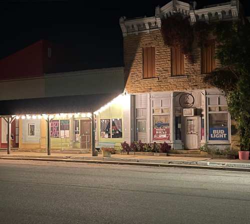 A quaint building at night, adorned with string lights, featuring a bar and a storefront with signs.