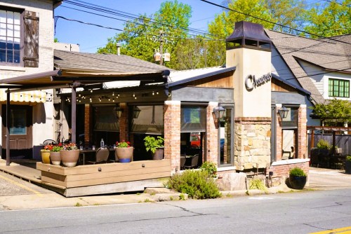 A charming restaurant exterior with a stone and brick facade, outdoor seating, and colorful flower pots.