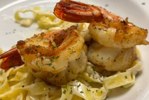 Two grilled shrimp on a bed of creamy fettuccine, garnished with herbs.