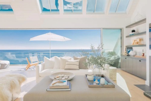 Bright, modern living room with a view of the ocean, featuring a white sofa, coffee table, and large glass doors.