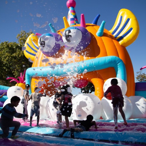Children play in a colorful foam-filled inflatable area, splashing and enjoying a sunny day.