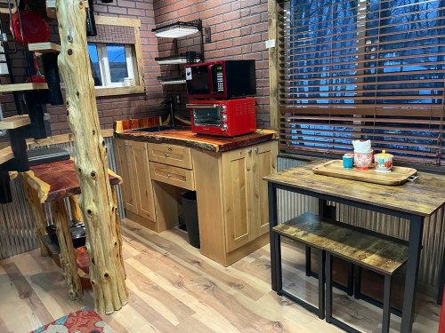 Cozy kitchen with wooden cabinets, a red microwave, and a small dining table by a window with blinds.