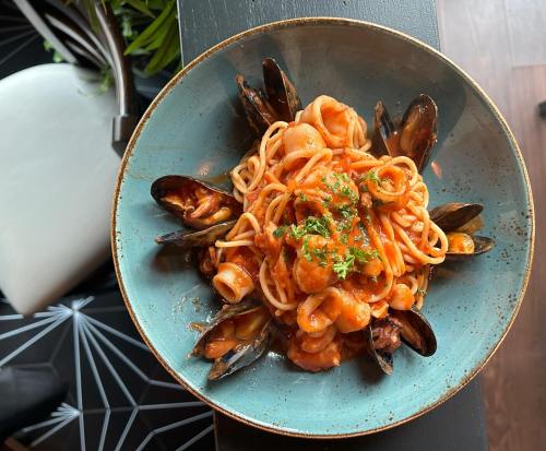 A blue plate filled with spaghetti topped with seafood, including mussels and shrimp, garnished with parsley.
