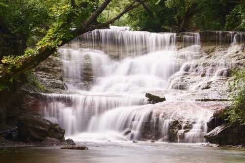 A serene waterfall cascading over rocky ledges, surrounded by lush greenery and a tranquil river below.