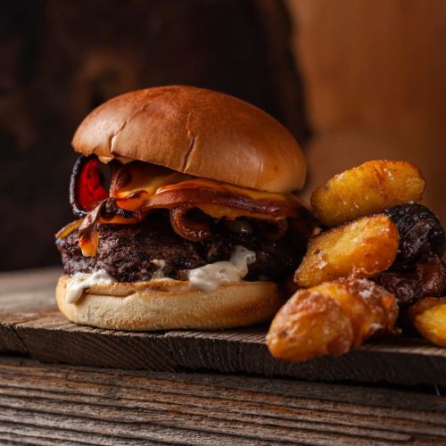 A juicy burger with melted cheese, grilled onions, and bacon, served with crispy potato wedges on a wooden surface.