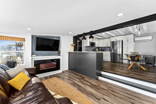 Cozy living space with a brown sofa, modern kitchen, and dining area, featuring wood floors and a fireplace.