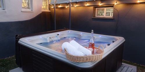A hot tub with glowing lights, towels in a basket, and a bottle of rosé, set in a cozy outdoor space.