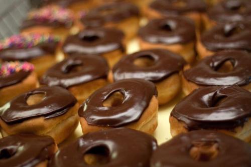 A close-up of freshly glazed chocolate donuts arranged in a neat row, some topped with colorful sprinkles.