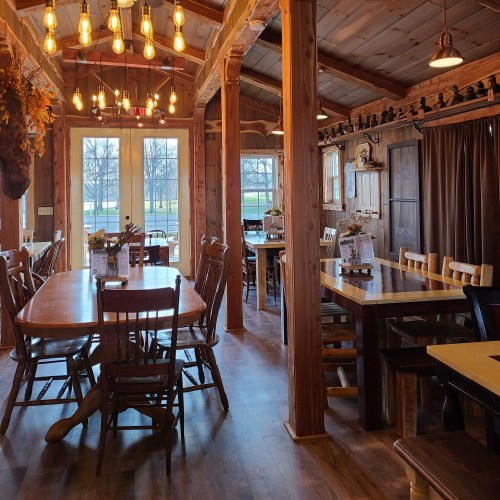 Cozy dining area with wooden tables, chairs, and warm lighting, featuring large windows overlooking a scenic view.