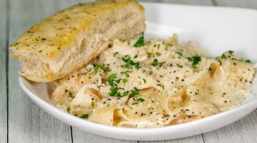 A plate of creamy pasta topped with parsley and grated cheese, accompanied by a slice of garlic bread.