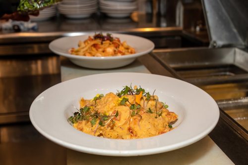 Two plates of pasta: one with creamy sauce and herbs, the other with a red sauce, in a restaurant kitchen setting.