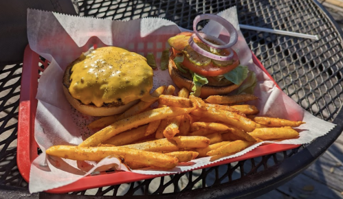 A cheeseburger with lettuce, tomato, and onion, served with a side of golden fries on a red tray.