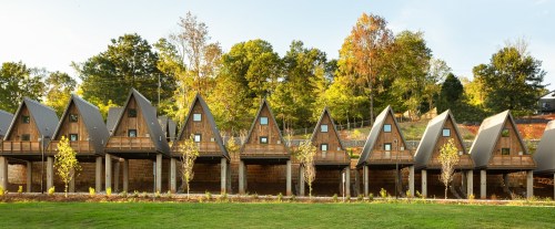A row of modern A-frame cabins set against a backdrop of trees and a clear sky.