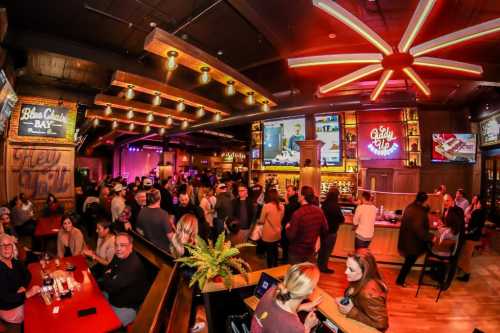 A lively bar scene with a crowd enjoying drinks, colorful lights, and a large screen displaying entertainment.