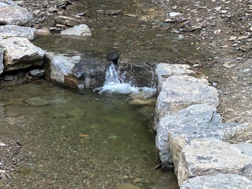 A small stream flows over rocks, creating a gentle waterfall in a natural setting.