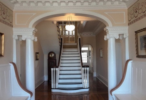 Elegant foyer with a grand staircase, decorative archways, and classic wooden details. Soft lighting enhances the ambiance.