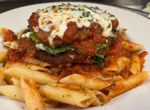 A plate of pasta topped with a breaded chicken patty, marinara sauce, melted cheese, and fresh spinach.