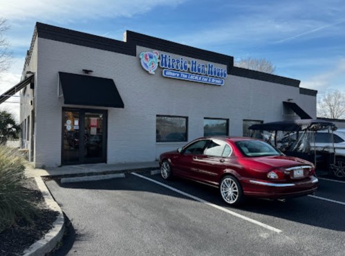 A red car parked outside a building with a sign that reads "Hippie Hen House" on a clear day.
