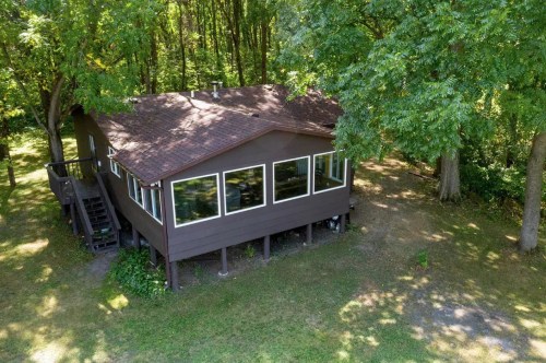 Aerial view of a brown house surrounded by trees, featuring large windows and a grassy yard.