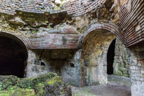 Ruins of an old stone structure with arched openings and moss-covered ground, showcasing weathered brickwork.