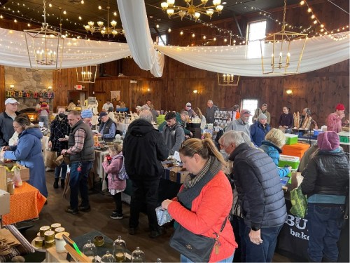 A bustling indoor market with people browsing various stalls, surrounded by festive decorations and warm lighting.