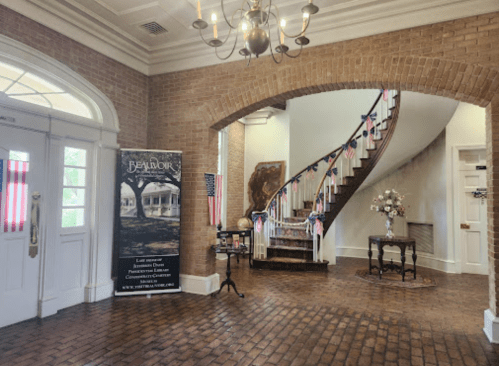 A spacious foyer with a staircase, brick walls, and patriotic decorations, featuring a banner for "Beauvoir."