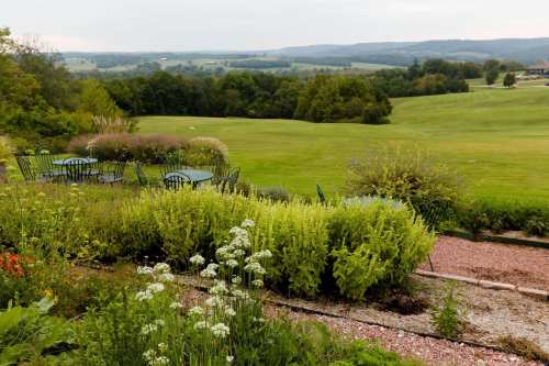 A scenic view of a green landscape with tables and chairs overlooking rolling hills and a cloudy sky.